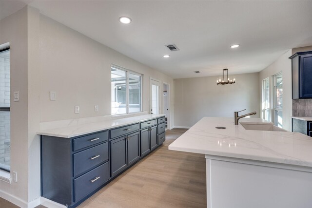 kitchen with light stone counters, an island with sink, and light wood-type flooring