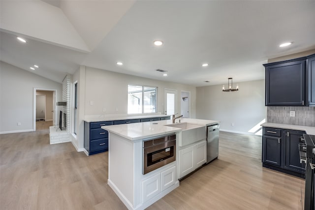 kitchen featuring an island with sink, appliances with stainless steel finishes, vaulted ceiling, light hardwood / wood-style floors, and sink