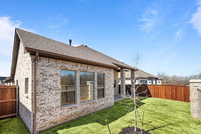 back of property featuring brick siding, a yard, a fenced backyard, and roof with shingles