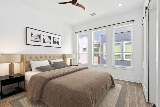 bedroom with light wood finished floors, a barn door, visible vents, baseboards, and recessed lighting