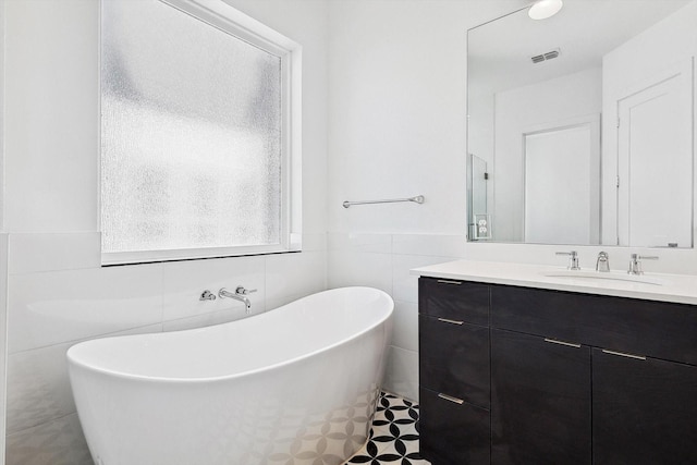 full bathroom featuring a soaking tub, vanity, visible vents, and tile walls