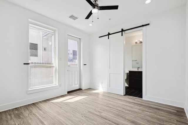 empty room with a barn door, visible vents, baseboards, ceiling fan, and light wood-type flooring