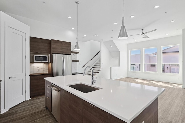 kitchen with an island with sink, appliances with stainless steel finishes, light countertops, and a sink