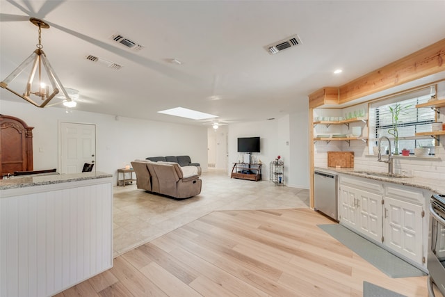 kitchen featuring light stone countertops, appliances with stainless steel finishes, decorative light fixtures, white cabinetry, and a skylight