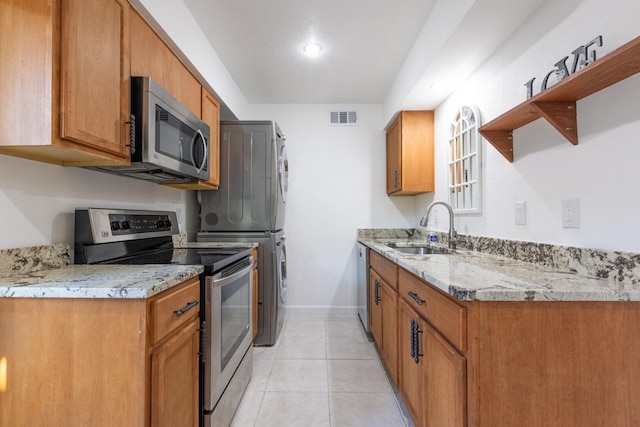 kitchen with light stone countertops, sink, stacked washer and dryer, and stainless steel appliances