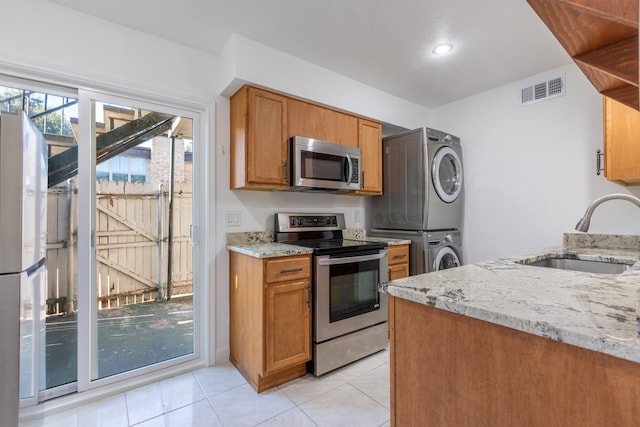 kitchen featuring stainless steel appliances, light stone counters, stacked washer / drying machine, and sink