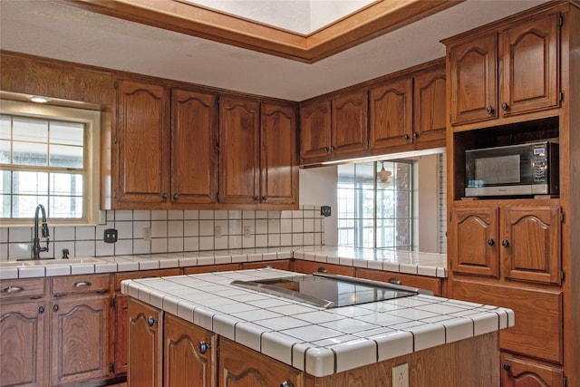 kitchen with sink, tile counters, black electric stovetop, and a kitchen island