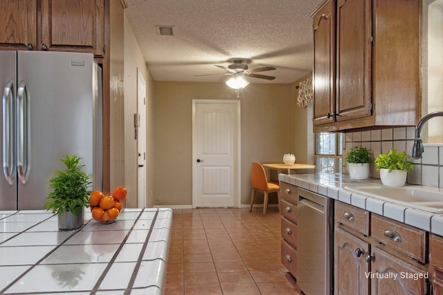 kitchen with appliances with stainless steel finishes, a textured ceiling, sink, light tile patterned floors, and tile countertops