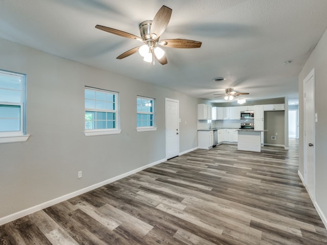 unfurnished living room featuring dark wood-type flooring and ceiling fan