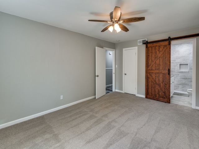 unfurnished bedroom featuring ceiling fan, ensuite bath, a barn door, and carpet