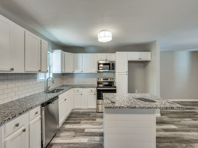 kitchen featuring sink, white cabinetry, appliances with stainless steel finishes, a center island, and light stone countertops