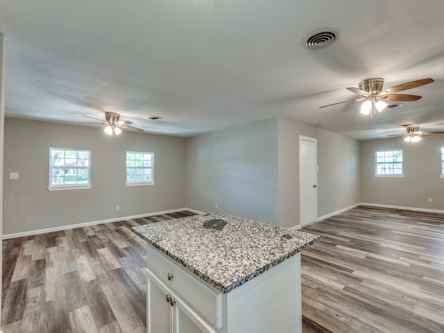 kitchen with light stone counters, a center island, white cabinets, light hardwood / wood-style flooring, and a textured ceiling