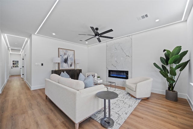 living room with ceiling fan, a premium fireplace, and light hardwood / wood-style floors