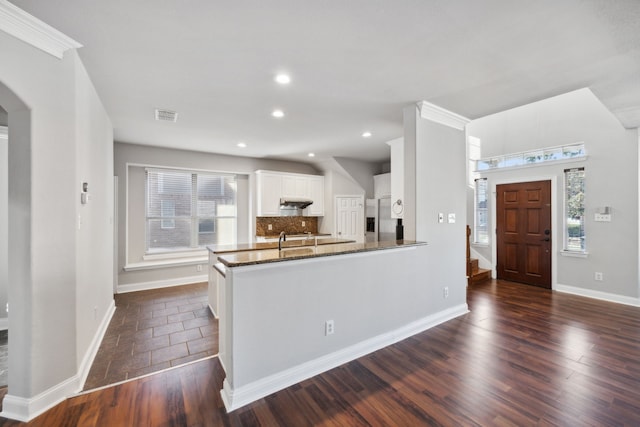 kitchen with visible vents, stainless steel refrigerator with ice dispenser, dark wood finished floors, arched walkways, and decorative backsplash