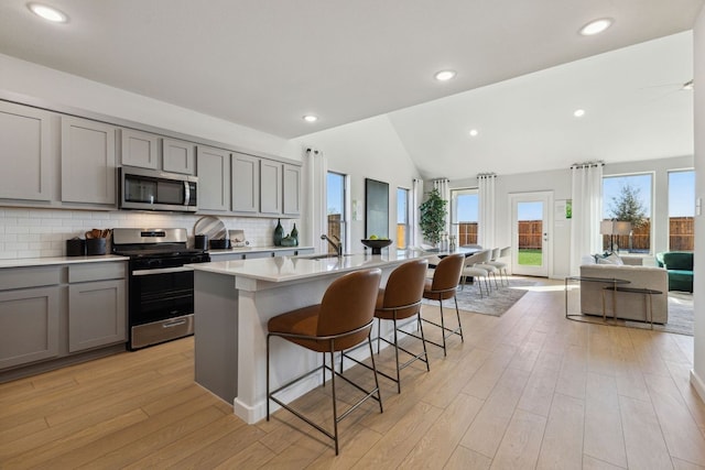 kitchen with light wood-type flooring, a kitchen island with sink, stainless steel appliances, vaulted ceiling, and a kitchen breakfast bar