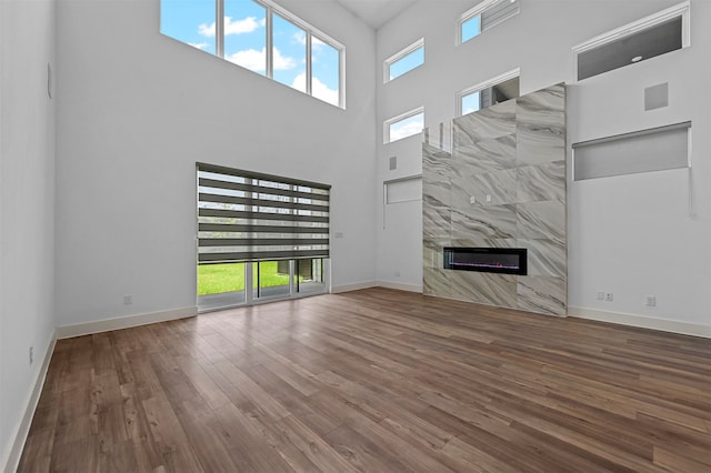 unfurnished living room featuring hardwood / wood-style floors, a healthy amount of sunlight, a high end fireplace, and a towering ceiling