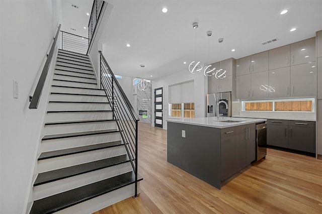 kitchen featuring light hardwood / wood-style floors, gray cabinets, stainless steel appliances, hanging light fixtures, and an island with sink