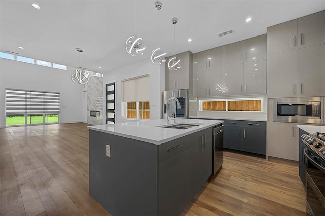 kitchen featuring a kitchen island with sink, gray cabinetry, sink, appliances with stainless steel finishes, and decorative light fixtures