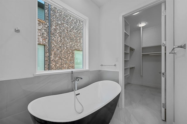 bathroom with a tub to relax in and tile walls