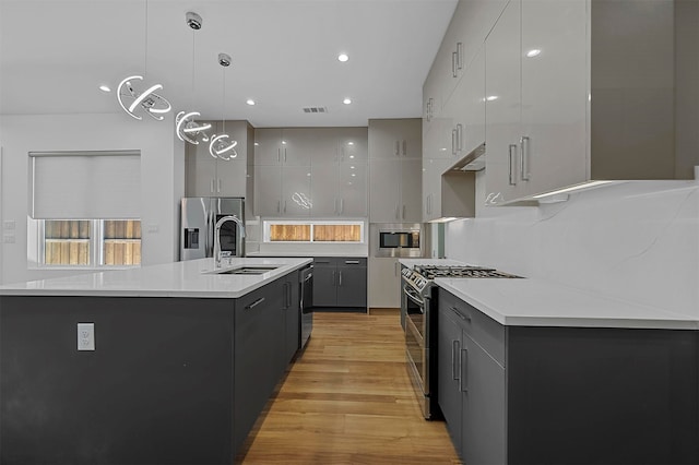 kitchen with an island with sink, stainless steel appliances, hanging light fixtures, and gray cabinetry