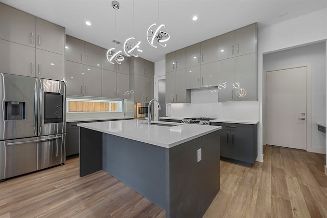 kitchen featuring pendant lighting, an island with sink, stainless steel refrigerator with ice dispenser, gray cabinets, and light wood-type flooring