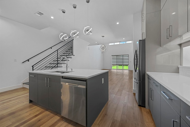 kitchen featuring pendant lighting, wood-type flooring, a center island with sink, gray cabinets, and stainless steel appliances