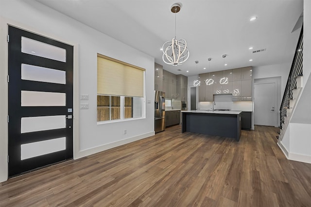 kitchen with gray cabinets, dark hardwood / wood-style floors, decorative light fixtures, an island with sink, and stainless steel fridge with ice dispenser