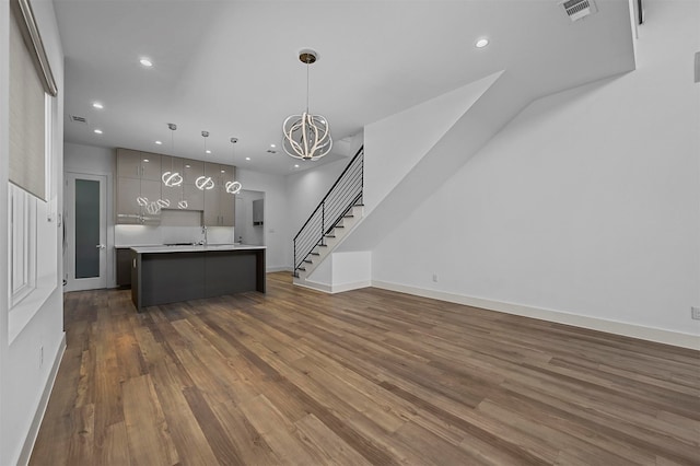 kitchen with a kitchen island with sink, dark wood-type flooring, sink, a notable chandelier, and decorative light fixtures