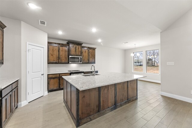 kitchen with an island with sink, sink, hanging light fixtures, stainless steel dishwasher, and light stone countertops