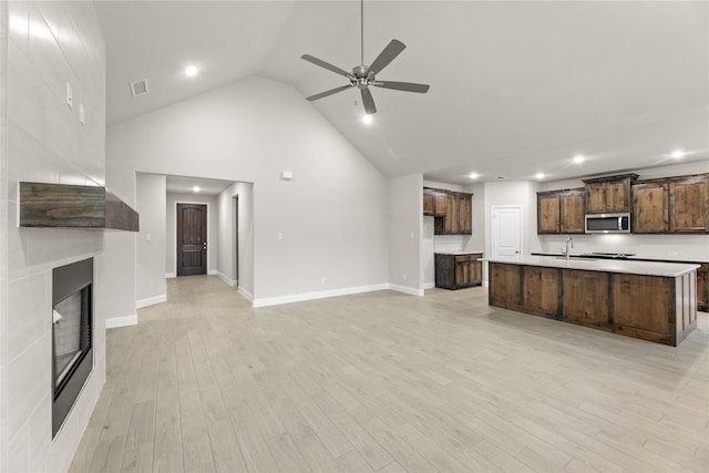 unfurnished living room featuring sink, high vaulted ceiling, ceiling fan, a fireplace, and light hardwood / wood-style floors