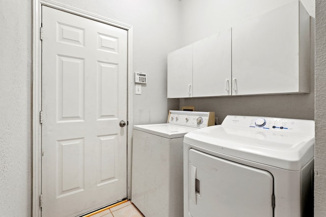 clothes washing area with cabinets, washer and dryer, and light tile patterned flooring