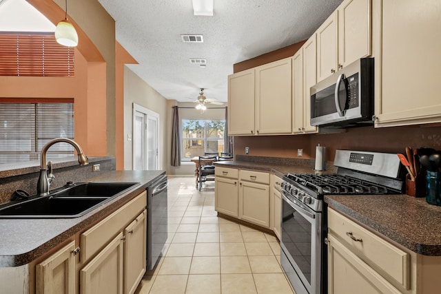 kitchen featuring a textured ceiling, stainless steel appliances, cream cabinetry, and sink