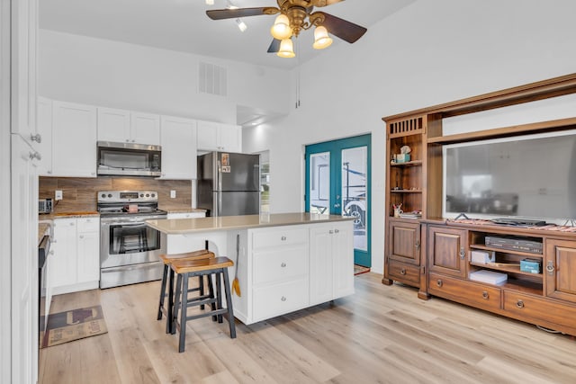 kitchen featuring a towering ceiling, white cabinetry, a center island, and stainless steel appliances