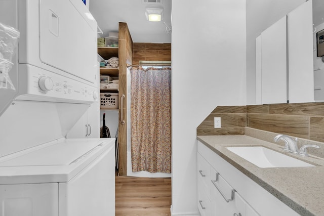 laundry room with stacked washer / drying machine, sink, and light hardwood / wood-style floors