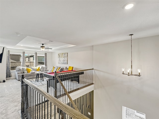 hall featuring a notable chandelier, a tray ceiling, and carpet flooring