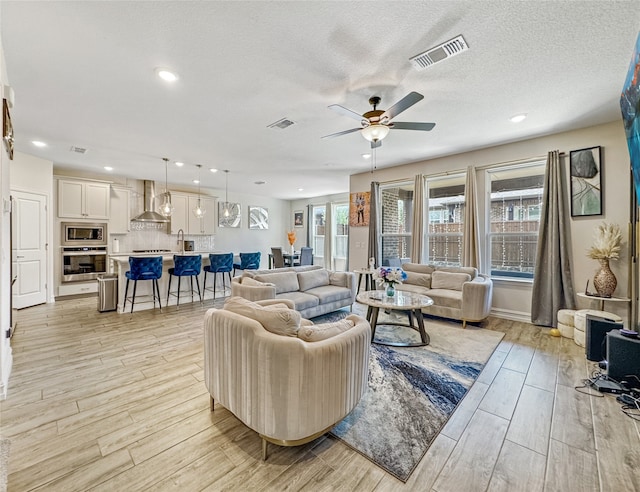 living room with light wood-type flooring, ceiling fan, sink, and a textured ceiling