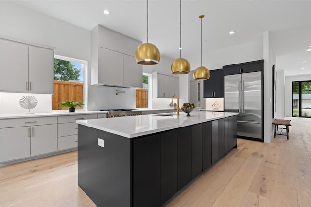 kitchen with light wood-type flooring, stainless steel appliances, white cabinets, hanging light fixtures, and a center island with sink