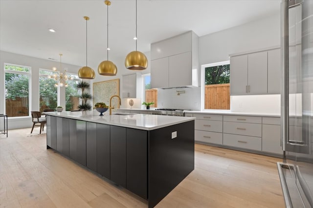 kitchen featuring a large island with sink, decorative light fixtures, sink, and light hardwood / wood-style flooring