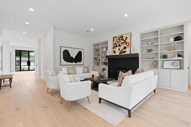 living room with a brick fireplace, light hardwood / wood-style flooring, and built in features