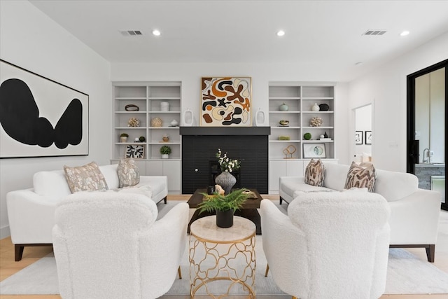 living room featuring a brick fireplace, light wood-type flooring, sink, and built in shelves