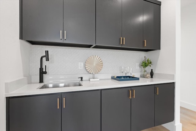 bar with decorative backsplash, gray cabinets, sink, and light wood-type flooring