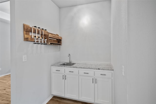 bar featuring white cabinetry, light stone countertops, sink, and hardwood / wood-style floors