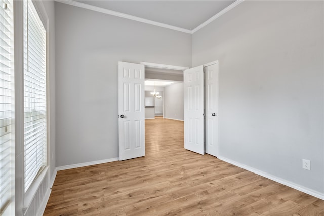 empty room with a wealth of natural light, crown molding, light wood-type flooring, and a chandelier