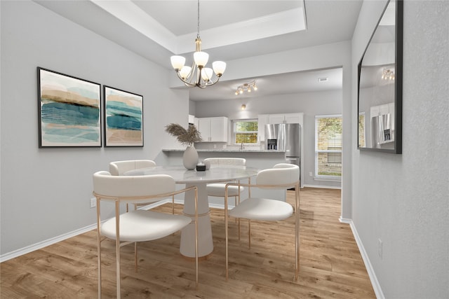 dining room with light hardwood / wood-style flooring, a chandelier, and a tray ceiling