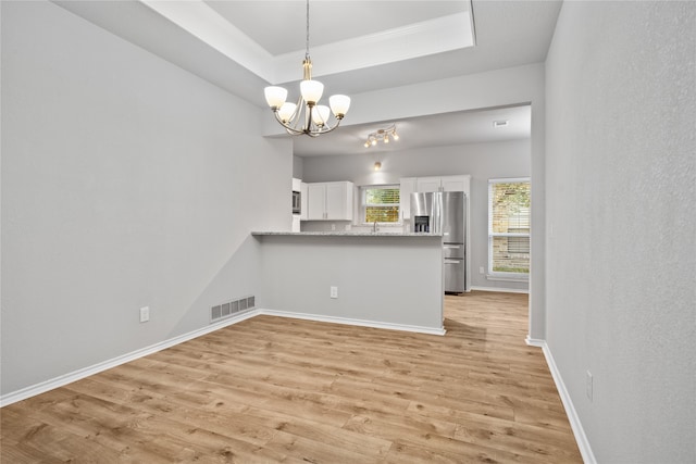 kitchen with light hardwood / wood-style flooring, kitchen peninsula, white cabinets, an inviting chandelier, and appliances with stainless steel finishes