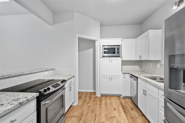 kitchen featuring white cabinetry, light stone counters, stainless steel appliances, and light wood-type flooring