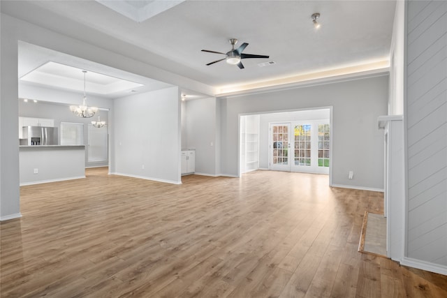 unfurnished living room with a tray ceiling, light hardwood / wood-style flooring, and ceiling fan with notable chandelier