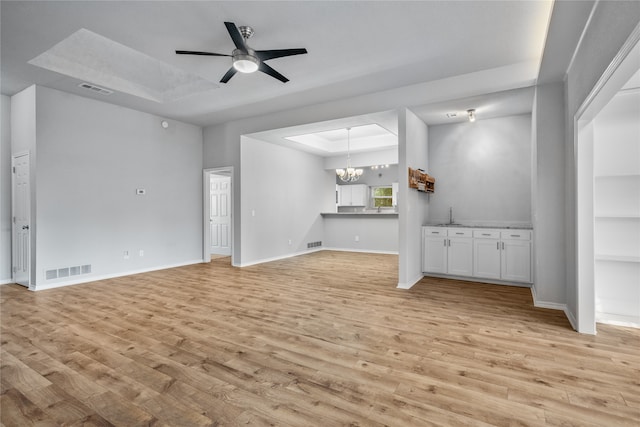 unfurnished living room featuring sink, ceiling fan with notable chandelier, light wood-type flooring, and a raised ceiling