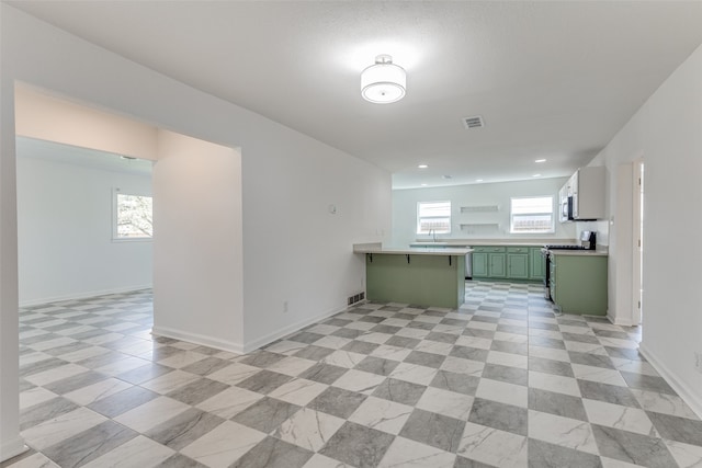 kitchen featuring a kitchen breakfast bar, sink, green cabinetry, kitchen peninsula, and appliances with stainless steel finishes