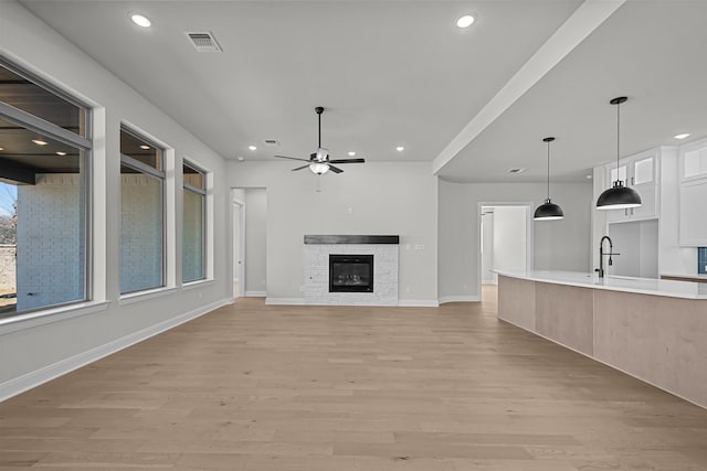 unfurnished living room featuring a stone fireplace, a ceiling fan, visible vents, and light wood finished floors